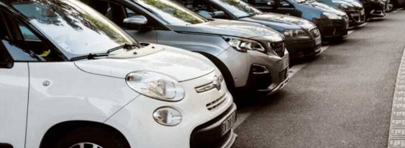 Zdjęcie przedstawia rząd zaparkowanych aut różnych marek wzdłuż ulicy, co może wiązać się z ryzykiem szkód parkingowych; pojazdy ustawione równolegle do chodnika, stwarzające typową scenę miejskiego parkowania.
