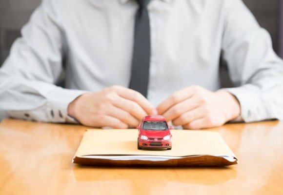 Mały czerwony samochodzik-zabawka stoi na dokumentach niezbędnych do opłacenia akcyzy za samochód.
