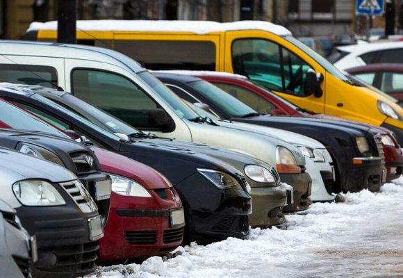 Przy ośnieżonym chodniku zaparkowane są różne rodzaje pojazdów