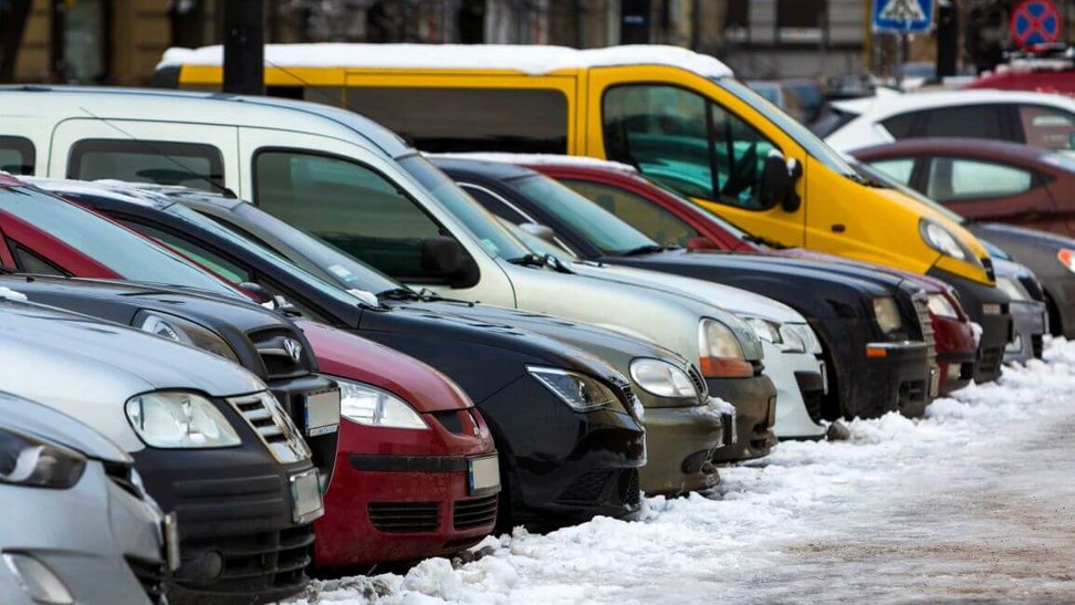 Przy ośnieżonym chodniku zaparkowane są różne rodzaje pojazdów