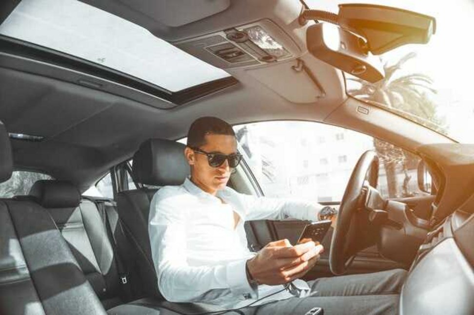 Mężczyzna w samochodzie sprawdza na telefonie wpływ cesji leasingu na ubezpieczenie