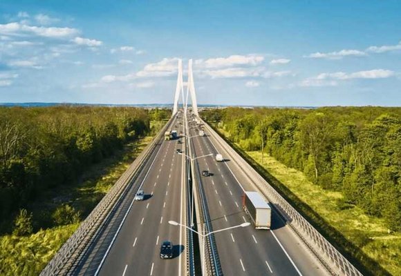 Widok na nowoczesny wielopasmowy autostradowy most z białymi kablami, po którym poruszają się różne pojazdy w obu kierunkach, z ciężarówką i samochodami osobowymi – potencjalny przykład drogi objętej systemem opłat drogowych eurowinieta