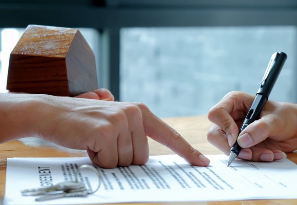 Dwie osoby podpisują umowę najmu okazjonalnego mieszkania, obok znajduje się miniaturowy model domu