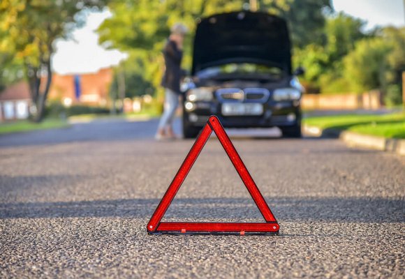 Na drodze stoi trójkąt ostrzegawczy, w tle widać uszkodzony samochód.