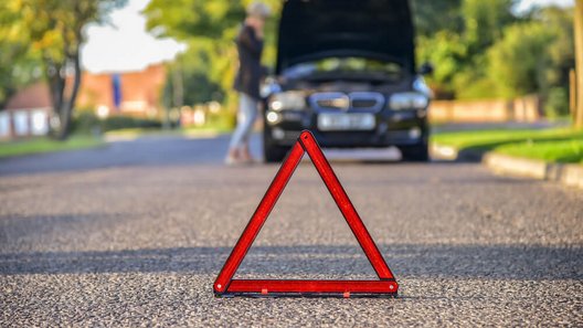 Na drodze stoi trójkąt ostrzegawczy, w tle widać uszkodzony samochód.
