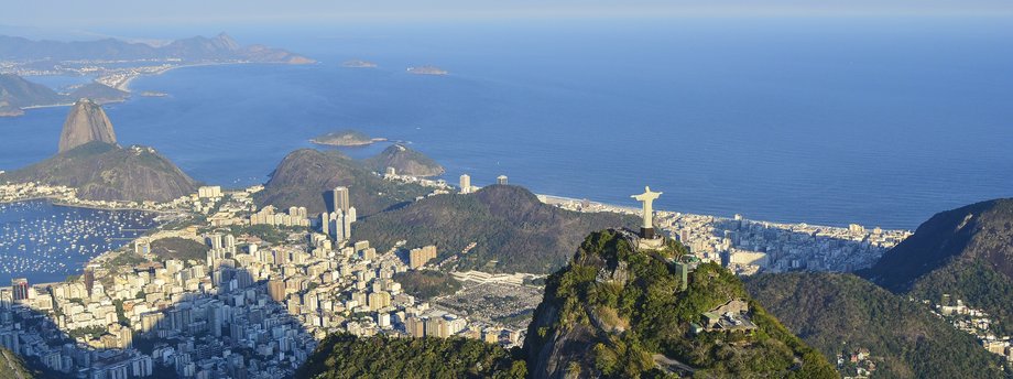 Widok z lotu ptaka na Rio de Janeiro z posągiem Chrystusa Odkupiciela na szczycie góry Corcovado, z panoramą miasta, mariną, górami i Oceanem Atlantyckim w tle.