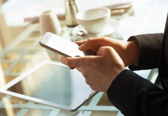 Osoba korzystająca ze smartfona przy stole, dla którego kupuje ubezpieczenie ekranu telefonu online