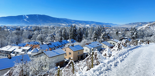 Zimowy krajobraz w Mariborze w Słowenii z ośnieżonymi domami, lasem i pasmem górskim w tle pod błękitnym niebem