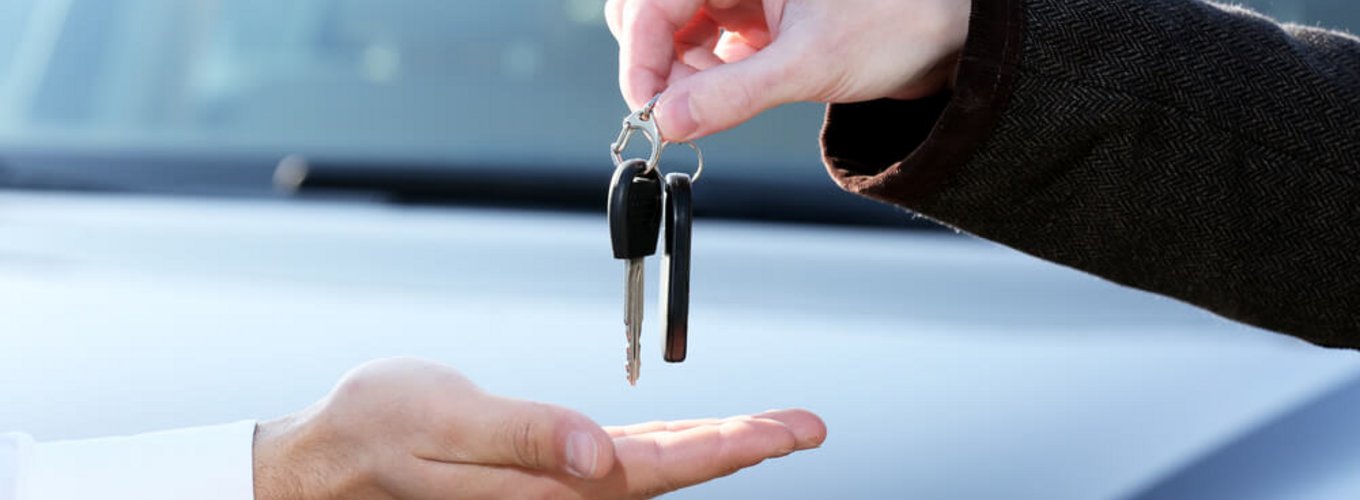 Przekazanie kluczyków na tle samochodu.