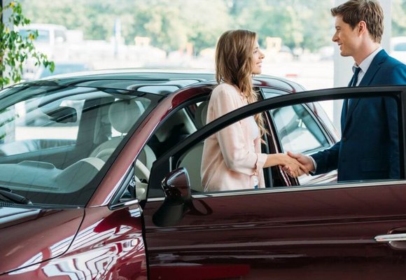 Kobieta i mężczyzna stoją przy samochodzie i zawierają umowę kupna-sprzedaży owego auta