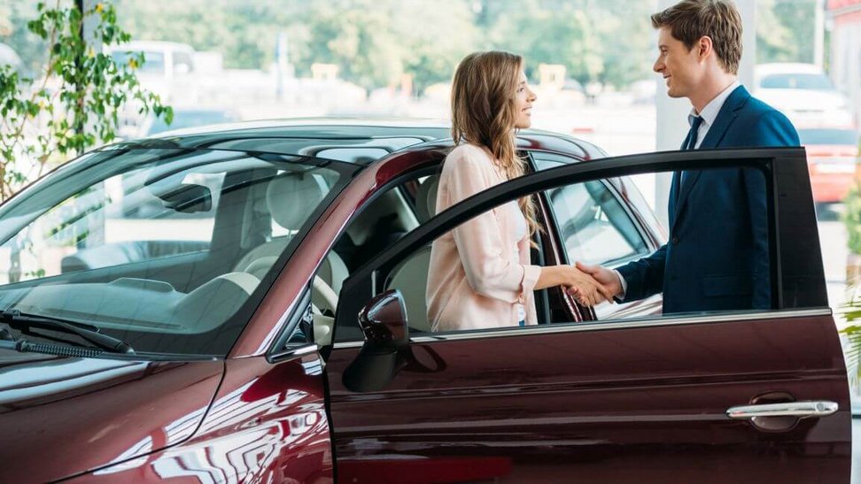 Kobieta i mężczyzna stoją przy samochodzie i zawierają umowę kupna-sprzedaży owego auta
