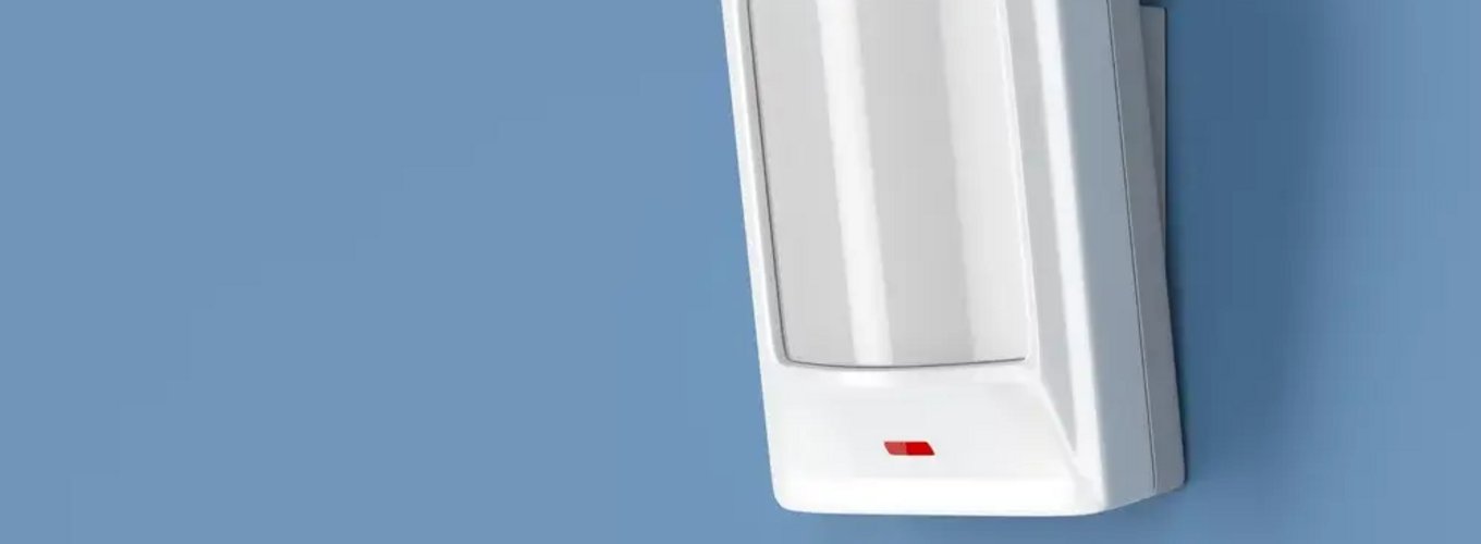 Nowoczesny biały czujnik ruchu zamontowany na gładkiej niebieskiej ścianie, używany do systemów bezpieczeństwa i automatyzacji w domach i biurach.