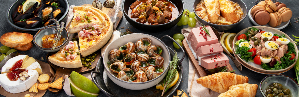 Różnorodne francuskie dania na stole, w tym małże, tosty z dżemem, deska serów, quiche, ślimaki, gulasz, tosty francuskie, makaroniki, pasztet, sałatka, rogaliki