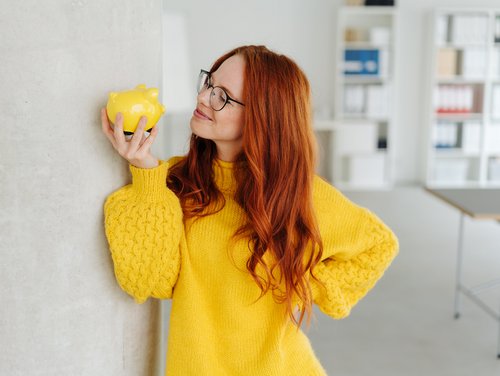 Smiling young woman contemplating a piggy bank