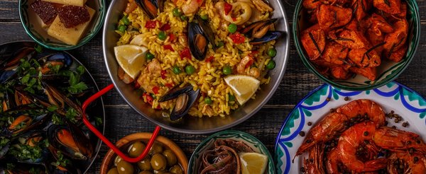 Apetyczny wybór hiszpańskich tapas z paellą z owocami morza na środku. Obok krewetki, małże i inne owoce morza