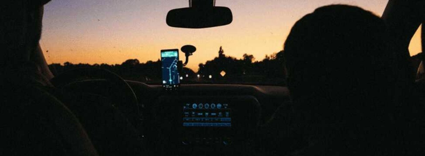Podróż samochodem do Chorwacji widać z perspektywy tylnej kanapy, skupiając się na dwóch pasażerach i kierowcy przed zmierzchem z nawigacją GPS włączoną na smartfonie.