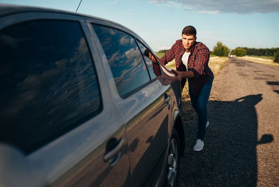 mężczyzna pcha zepsute auto