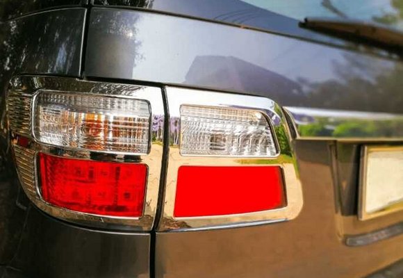 Zbliżenie na światła pozycyjne samochodu, przedstawiające jasną lampę kierunkowskazu i czerwoną lampę światła stop na tle metalicznego lakieru pojazdu, z rozmytym lustrzanym odbiciem otoczenia.