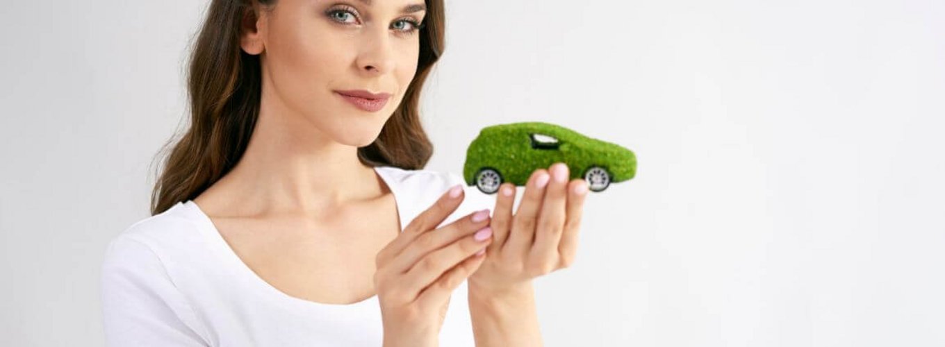 Kobieta trzyma w ręku miniaturkę elektrycznego samochodu z zielonymi tablicami rejestracyjnymi