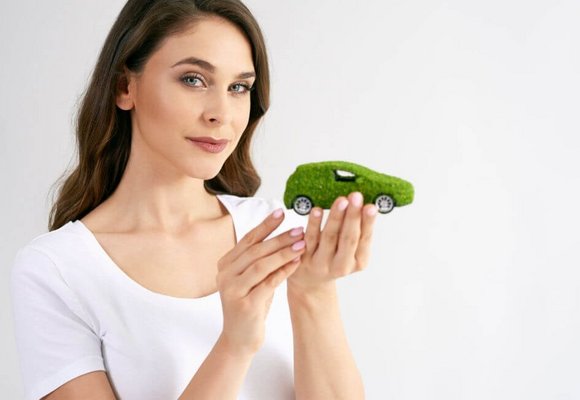 Kobieta trzyma w ręku miniaturkę elektrycznego samochodu z zielonymi tablicami rejestracyjnymi