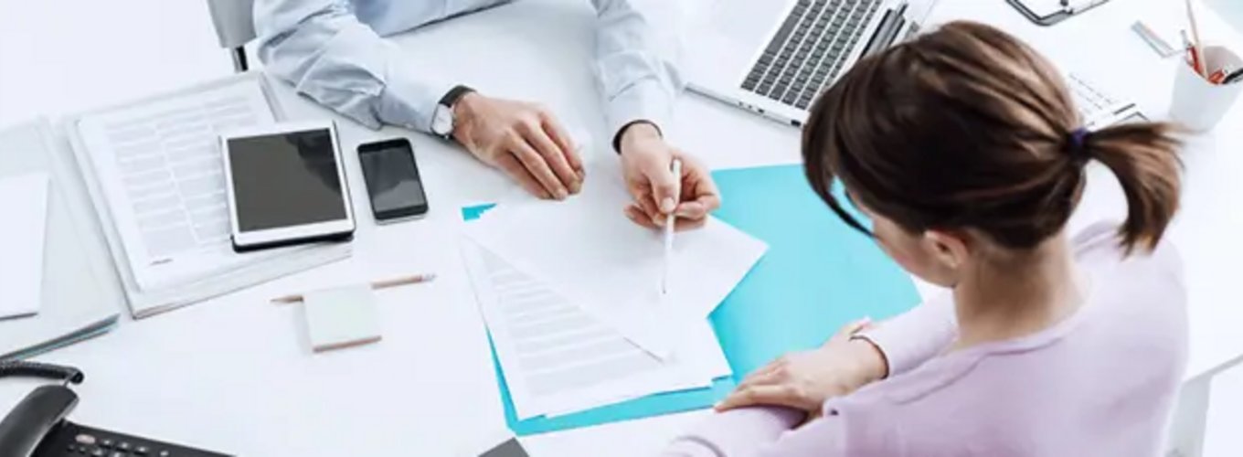 Dwie osoby pracujące przy biurku z dokumentami, laptopem, tabletami i smartfonami, mężczyzna wskazuje na dokument, który analizuje kobieta w rozważnym geście. Dwie osoby pracujące przy biurku z dokumentami, laptopem, tabletami i smartfonami, mężczyzna wskazuje na dokument, który analizuje kobieta w rozważnym geście.