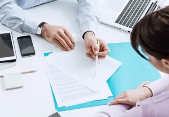 Dwie osoby pracujące przy biurku z dokumentami, laptopem, tabletami i smartfonami, mężczyzna wskazuje na dokument, który analizuje kobieta w rozważnym geście. Dwie osoby pracujące przy biurku z dokumentami, laptopem, tabletami i smartfonami, mężczyzna wskazuje na dokument, który analizuje kobieta w rozważnym geście.