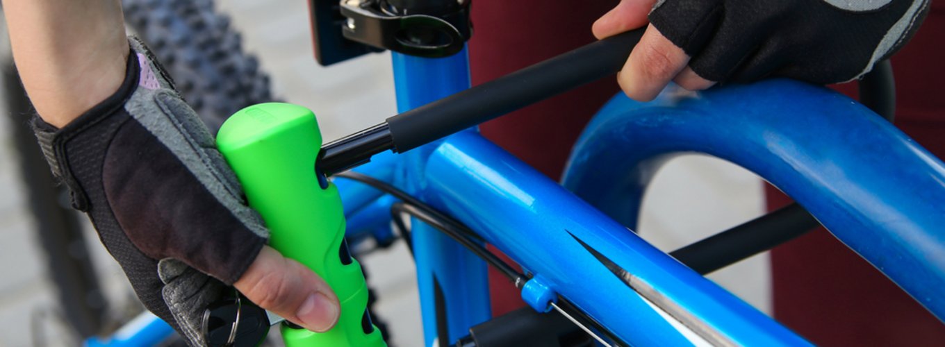 Osoba zabezpieczająca rower przed kradzieżą, która za pomocą zapięcia U-lock przypina rower do stojaka rowerowego. Właściciel roweru zabezpiecza swój rower przed kradzieżą za pomocą zapięcia typu U-lock