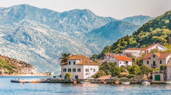 Kobieta wędruje kamienną ścieżką z widokiem na malowniczą zatokę i miasto Kotor w Czarnogórze - idealne miejsce na aktywne wakacje z ubezpieczeniem turystycznym