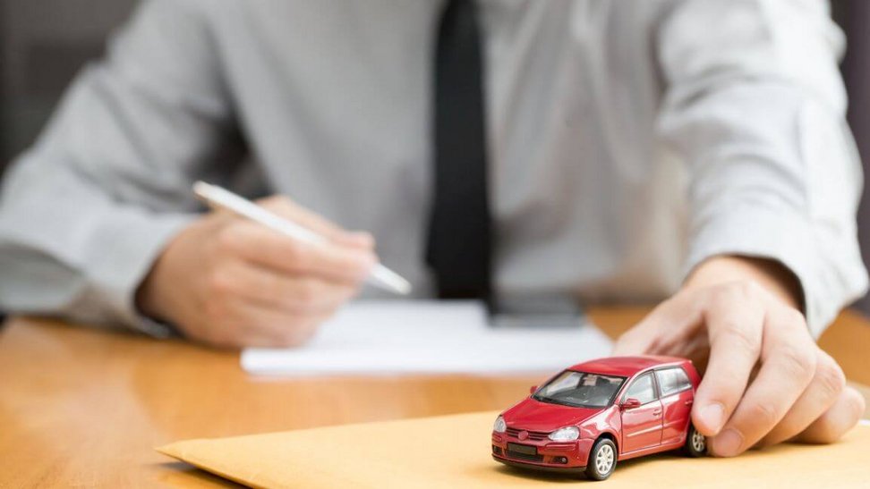 Mężczyzna trzyma w lewej ręce mini auto, a drugą ręką podpisuje dokumenty na mini AC
