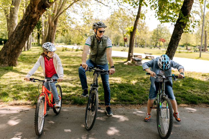 Rodzina jedzie na rowerach po parku, zatrzymując się na ścieżce wśród drzew i zielen Rodzina jedzie na rowerach po parku, zatrzymując się na ścieżce wśród drzew i zielen