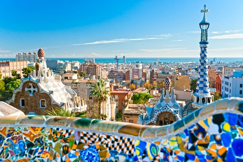 Park Güell w Barcelonie z kolorowymi mozaikami, charakterystycznymi dla projektów Antoniego Gaudíego, oraz panoramą miasta w tle.