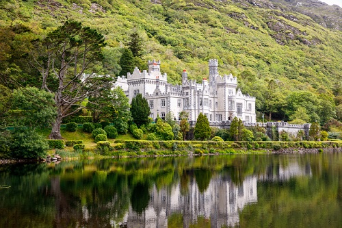 kylemore, Irlandia zamek, położony nad spokojnym zbiornikiem wodnym, z odbiciem budynku na powierzchni wody, otoczony bujną zielenią i drzewami, z zielonymi wzgórzami w tle
