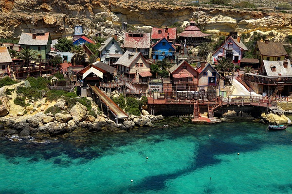 Kolorowe domki rybackie nad turkusową wodą w zatoce Popeye Village, jednej z najpopularniejszych atrakcji turystycznych Malty.
