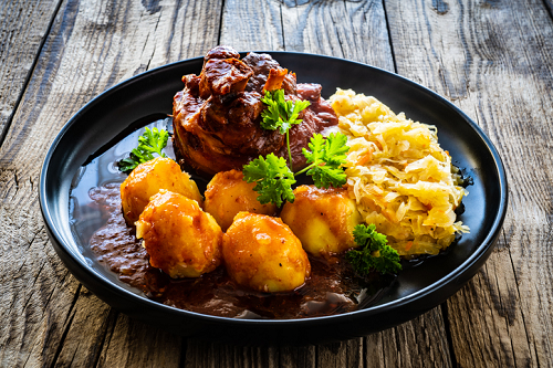 Tradycyjny obiad Schweinshaxe, ziemniakami w sosie i kiszoną kapustą – domowa kuchnia na drewnianym stole