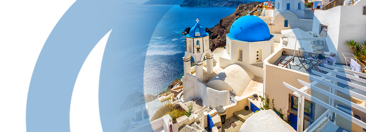 Widok na Santorini w Grecji, z charakterystycznymi białymi budynkami z niebieskimi kopułami, które górują nad Morzem Egejskim. W tle widać klify oraz dodatkowe budynki na zboczu wzgórza.
