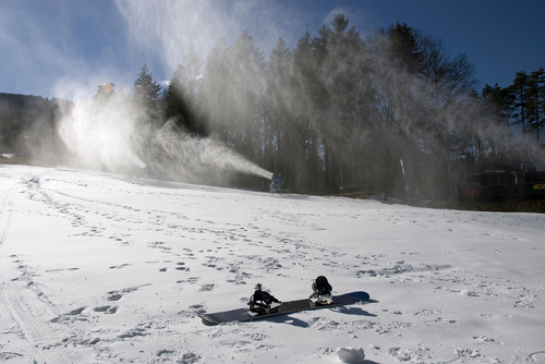 Stok narciarski z armatką śnieżną – śnieg, snowboardy na śniegu, zimowy krajobraz z lasem i błękitnym niebem