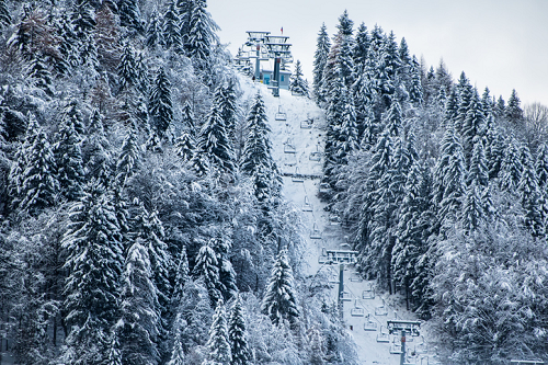 Zimowy krajobraz górski z wyciągiem narciarskim – ośnieżone stoki, las iglasty i stacja narciarska na szczycie