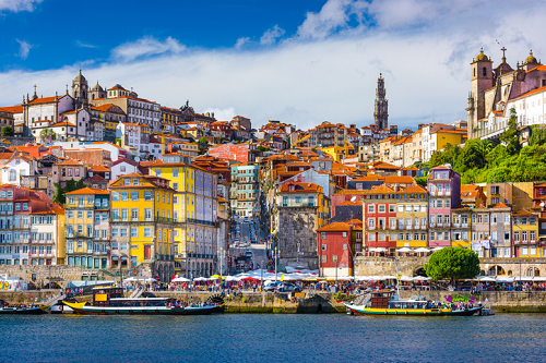 Kolorowy pejzaż Porto z rzeką Douro i tradycyjnymi łodziami Rabelo na tle historycznej architektury miasta.