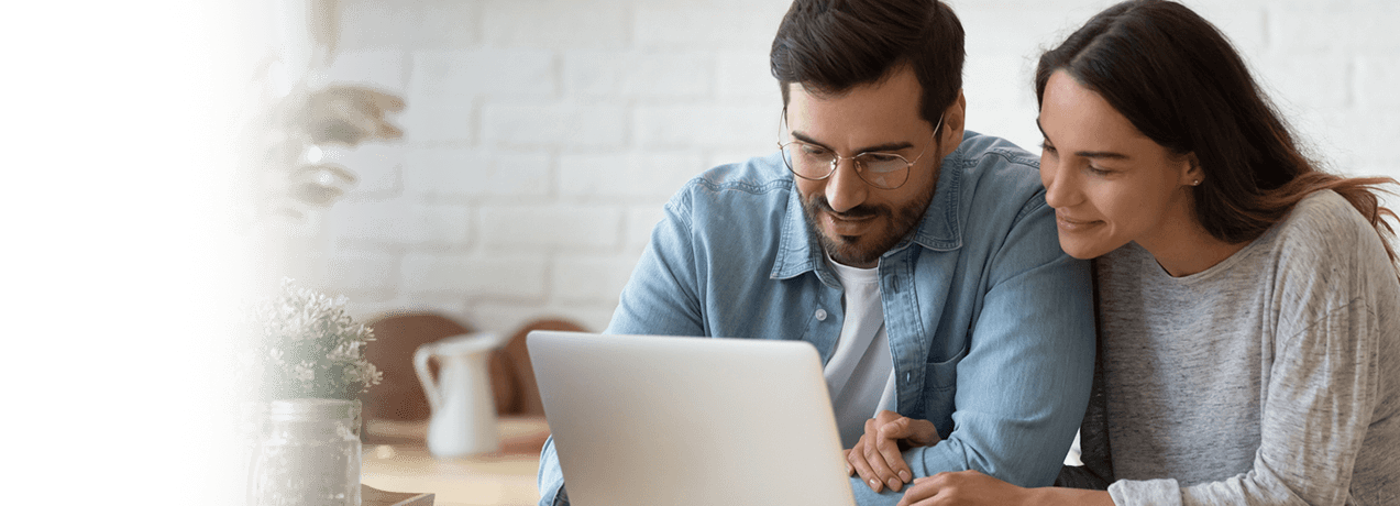 Uśmiechnięci mężczyzna i kobieta siedzą blisko siebie, patrząc na ekran laptopa