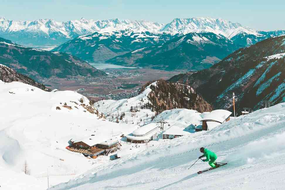 narciarz zjeżdżający ze stoku, w tle ośrodek narciarski w górach
