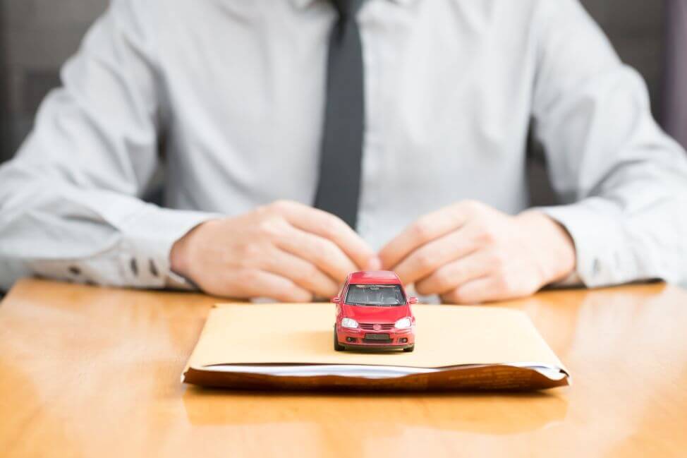 Mały czerwony samochodzik-zabawka stoi na dokumentach niezbędnych do opłacenia akcyzy za samochód.