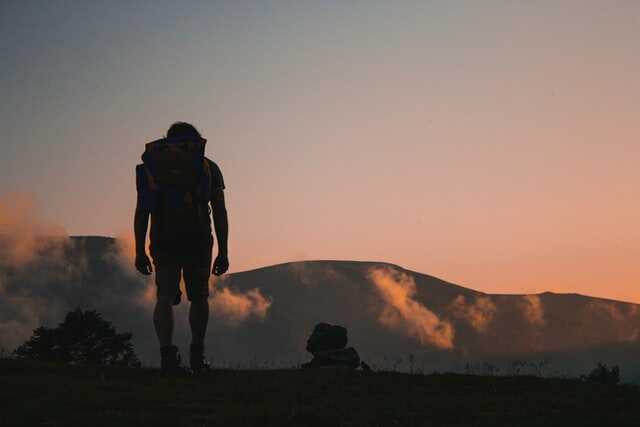 mężczyzna z plecakiem stojący tyłem na górskim szlaku