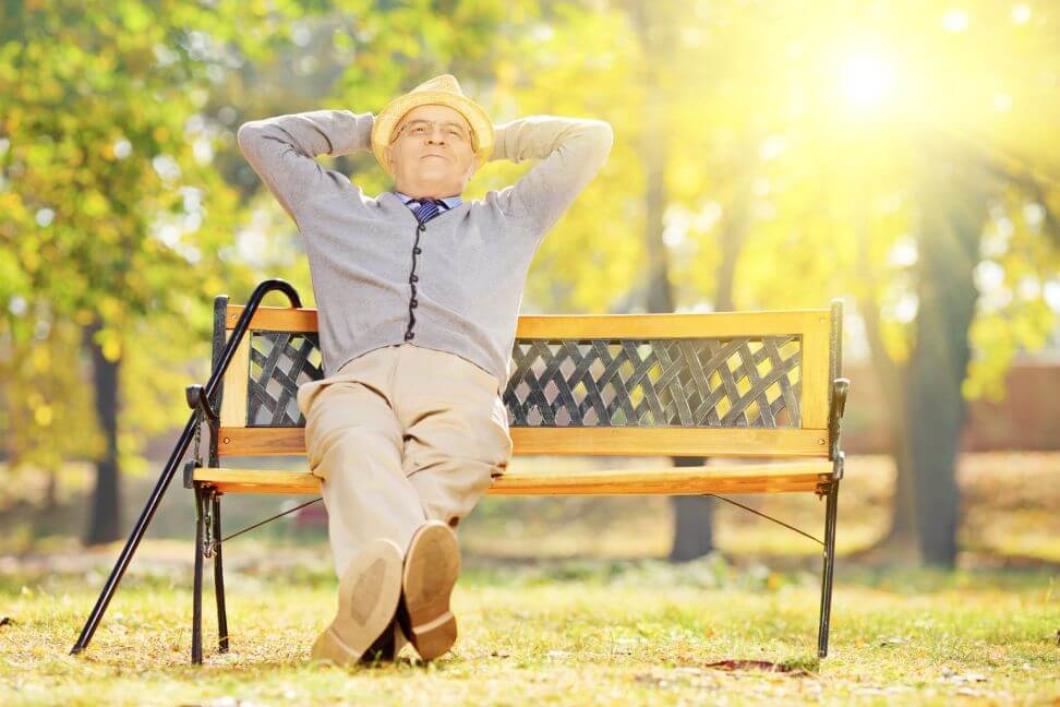 Starszy mężczyzna siedzi zrelaksowany na ławce w parku, nie boi się o swoją przyszłość ponieważ obejmuje go ubezpieczenie emerytalne
